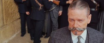Movie still from “Murder on the Orient Express” (2017), directed by Kenneth Branagh – An older man in a suit and tie with other men; Close Up shot, Over the shoulder angle