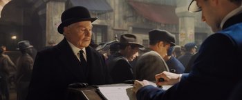 Movie still from “Murder on the Orient Express” (2017), directed by Kenneth Branagh – An old man wearing a suit and a hat sitting at a table; Medium shot, Over the shoulder angle