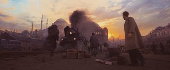 Movie still from “Murder on the Orient Express” (2017), directed by Kenneth Branagh – A train traveling down train tracks next to a building; Extreme Wide shot, Low angle