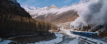 Movie still from “Murder on the Orient Express” (2017), directed by Kenneth Branagh – A train traveling down tracks next to snow covered mountains; Extreme Wide shot, Low angle