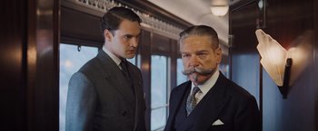 Movie still from “Murder on the Orient Express” (2017), directed by Kenneth Branagh – Two men in suits stand next to each other; Medium shot, Over the shoulder angle