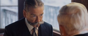 Movie still from “Murder on the Orient Express” (2017), directed by Kenneth Branagh – An older man wearing a suit and tie with a fake mustache; Close Up shot, Over the shoulder angle
