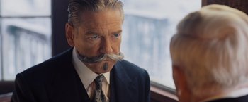 Movie still from “Murder on the Orient Express” (2017), directed by Kenneth Branagh – A person wearing a suit and tie; Close Up shot, Over the shoulder angle