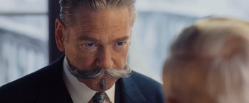 Movie still from “Murder on the Orient Express” (2017), directed by Kenneth Branagh – An older man wearing a suit and tie with a mustache; Close Up shot, Over the shoulder angle