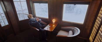 Movie still from “Murder on the Orient Express” (2017), directed by Kenneth Branagh – A man sitting in a chair in front of a window; Wide shot, High angle