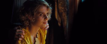 Movie still from “Murder on the Orient Express” (2017), directed by Kenneth Branagh – A beautiful woman with curly blonde hair wearing a necklace of yellow flowers; Close Up shot, Over the shoulder angle