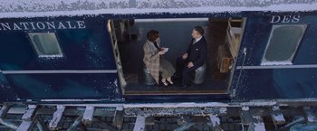 Movie still from “Murder on the Orient Express” (2017), directed by Kenneth Branagh – A man and a woman are sitting on a train platform; Wide shot, Overhead angle