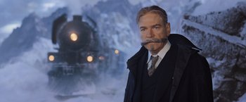 Movie still from “Murder on the Orient Express” (2017), directed by Kenneth Branagh – A man with a long mustache standing in front of a train; Medium shot, Low angle