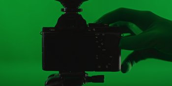Movie still from “My Fake Boyfriend” (2022), directed by Rose Troche – A person holding a camera up to a green screen; Extreme Close Up shot, Overhead angle