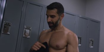 Movie still from “My Fake Boyfriend” (2022), directed by Rose Troche – A man with a beard is holding a towel in a locker room; Medium shot, Over the shoulder angle