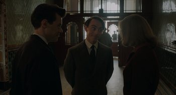 Movie still from “My Policeman” (2022), directed by Michael Grandage – A man and two women standing next to each other in a room; Medium shot, Over the shoulder angle