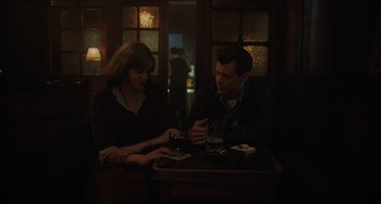 Movie still from “My Policeman” (2022), directed by Michael Grandage – A man and a woman sitting at a table with drinks; Medium shot, Over the shoulder angle