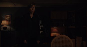 Movie still from “My Policeman” (2022), directed by Michael Grandage – A man standing in the dark in front of a lamp; Medium shot, Over the shoulder angle