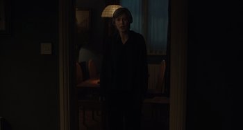 Movie still from “My Policeman” (2022), directed by Michael Grandage – A woman standing in a dark room in front of a lamp; Medium shot, Over the shoulder angle