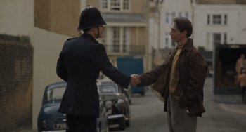 Movie still from “My Policeman” (2022), directed by Michael Grandage – Two men shaking hands on the side of the street; Medium shot, Over the shoulder angle