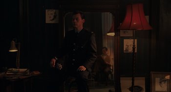 Movie still from “My Policeman” (2022), directed by Michael Grandage – A man in a uniform sitting in front of a mirror in a room; Medium shot, Over the shoulder angle