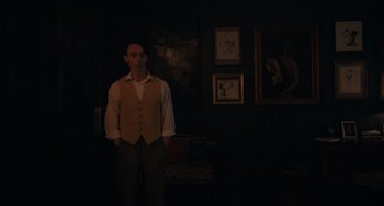 Movie still from “My Policeman” (2022), directed by Michael Grandage – A man standing in a dark room in front of pictures; Medium shot, Over the shoulder angle