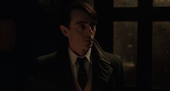 Movie still from “My Policeman” (2022), directed by Michael Grandage – A man wearing a suit and tie in a dark room; Close Up shot, Low angle