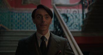 Movie still from “My Policeman” (2022), directed by Michael Grandage – A man in a suit and tie standing in front of a staircase; Close Up shot, Low angle