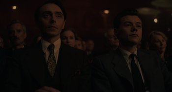 Movie still from “My Policeman” (2022), directed by Michael Grandage – Two men in suits and ties in a dark room; Medium shot, Low angle