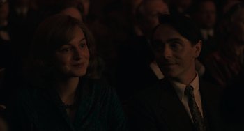 Movie still from “My Policeman” (2022), directed by Michael Grandage – A man and a woman sitting next to each other in front of a crowd; Medium shot, Over the shoulder angle