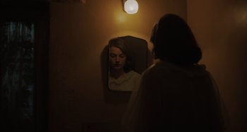 Movie still from “My Policeman” (2022), directed by Michael Grandage – A woman looking at her reflection in a mirror; Medium shot, Over the shoulder angle