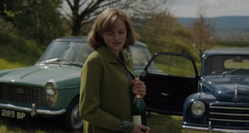 Movie still from “My Policeman” (2022), directed by Michael Grandage – A woman holding a bottle of wine in her hand; Medium shot, Over the shoulder angle