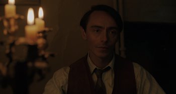 Movie still from “My Policeman” (2022), directed by Michael Grandage – A man wearing a vest and tie in a dimly - lit room; Close Up shot, Over the shoulder angle