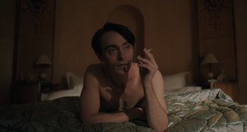 Movie still from “My Policeman” (2022), directed by Michael Grandage – A man laying on a bed smoking a cigarette; Medium shot, High angle