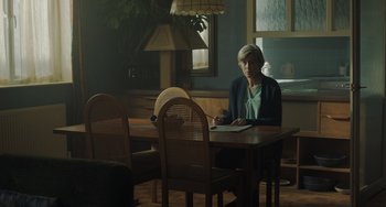 Movie still from “My Policeman” (2022), directed by Michael Grandage – An older woman sitting at a dining room table writing; Medium shot, Over the shoulder angle