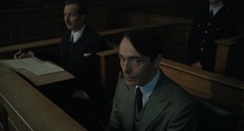 Movie still from “My Policeman” (2022), directed by Michael Grandage – A man in a suit and tie sitting in front of a judge; Close Up shot, Low angle