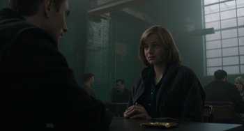 Movie still from “My Policeman” (2022), directed by Michael Grandage – A woman sitting at a table talking to another person; Medium shot, Over the shoulder angle
