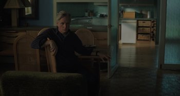 Movie still from “My Policeman” (2022), directed by Michael Grandage – A man sitting in a chair in a room; Medium shot, Over the shoulder angle