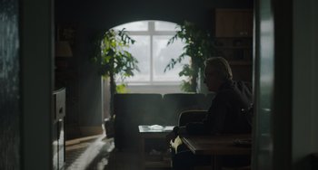 Movie still from “My Policeman” (2022), directed by Michael Grandage – A person sitting in a living room with a book; Wide shot, Over the shoulder angle