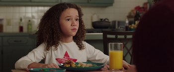 Movie still from “My Spy” (2020), directed by Peter Segal – A young girl sitting at a table in front of a plate of food and a glass of orange juice; Close Up shot, Over the shoulder angle