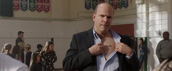 Movie still from “My Spy” (2020), directed by Peter Segal – A bald man in a suit is putting on his shirt; Close Up shot, Over the shoulder angle