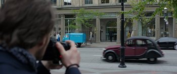 Movie still from “My Spy” (2020), directed by Peter Segal – A man taking a picture of a street scene with a blue truck; Wide shot, Over the shoulder angle