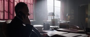Movie still from “My Spy” (2020), directed by Peter Segal – A man sitting at a desk in front of a large window; Medium shot, Low angle