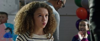 Movie still from “My Spy” (2020), directed by Peter Segal – A young girl with curly brown hair looking at the camera with a man standing behind her; Close Up shot, Over the shoulder angle