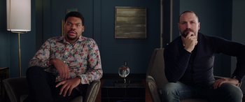 Movie still from “My Spy” (2020), directed by Peter Segal – A man sitting on a chair in a room; Medium shot, High angle