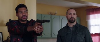 Movie still from “My Spy” (2020), directed by Peter Segal – A man holding a gun in front of another man in a kitchen; Medium shot, Low angle