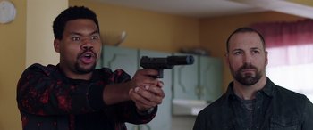 Movie still from “My Spy” (2020), directed by Peter Segal – A man holding a gun in a room with other people; Close Up shot, Over the shoulder angle