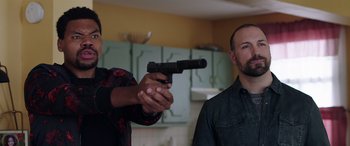 Movie still from “My Spy” (2020), directed by Peter Segal – A man holding a gun pointed at another man in a kitchen; Medium shot, Over the shoulder angle