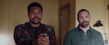 Movie still from “My Spy” (2020), directed by Peter Segal – Two men are holding guns in a living room; Medium shot, Over the shoulder angle