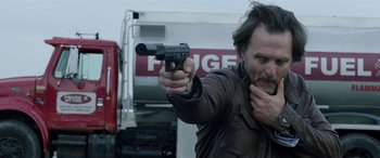 Movie still from “My Spy” (2020), directed by Peter Segal – A man holding a gun in front of a truck; Close Up shot, Over the shoulder angle