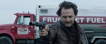 Movie still from “My Spy” (2020), directed by Peter Segal – A man holding a gun in front of a truck; Close Up shot, Low angle