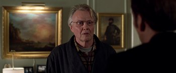Movie still from “National Treasure” (2004), directed by Jon Turteltaub – An older man wearing glasses in a room with paintings on the wall; Medium shot, Over the shoulder angle