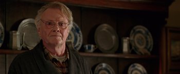 Movie still from “National Treasure” (2004), directed by Jon Turteltaub – An older man wearing glasses in front of plates; Close Up shot, Over the shoulder angle