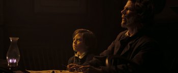 Movie still from “National Treasure: Book of Secrets” (2007), directed by Jon Turteltaub – A man sitting next to a young boy in a dark room; Medium shot, Over the shoulder angle