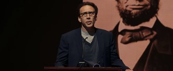Movie still from “National Treasure: Book of Secrets” (2007), directed by Jon Turteltaub – A man standing at a podium in front of a microphone; Close Up shot, Low angle